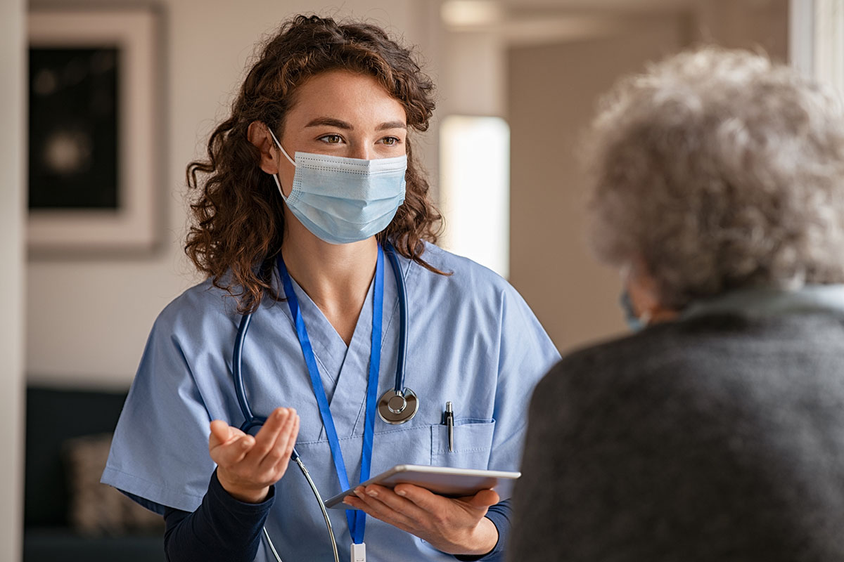 A female health care worker wearing a face mask speaks with a patient.