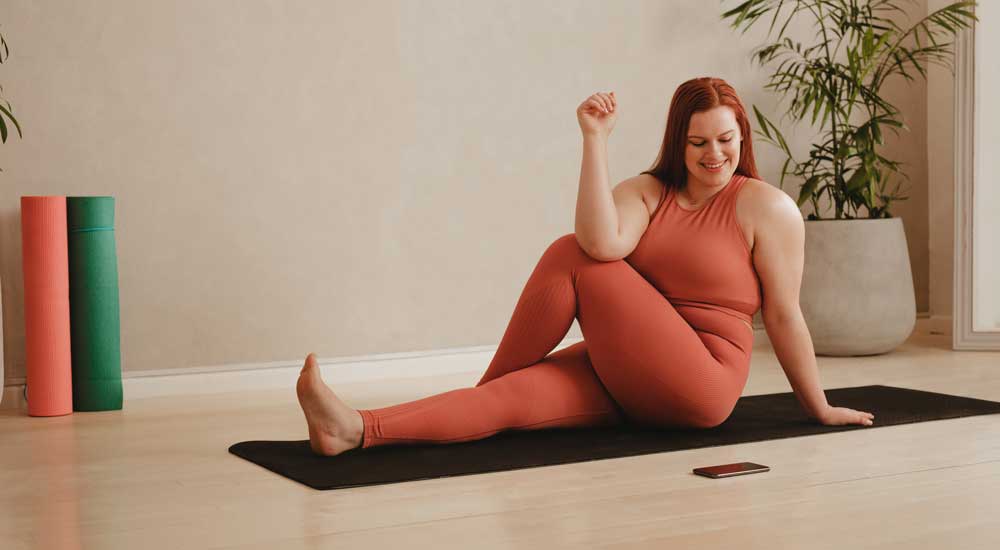 Woman on yoga mat stretching while looking at phone